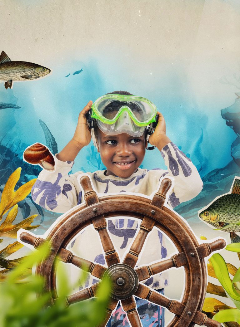 Lapsi jolla on snorkkeleiden uimalasit otsalla, seisoo ruorin takana vedenalaisessa maisemassa. Kuva on leikekirjamainen.