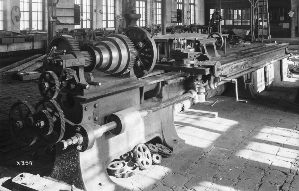 Vanhoja isoja koneita tehdashallissa, mustavalkoinen kuva.