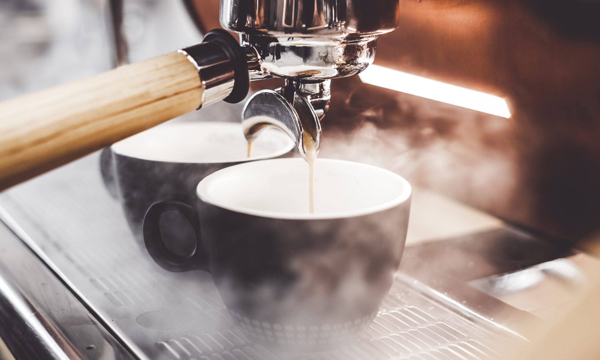 Kahteen kuppiin valuu kuumaa juotavaa kahviautomaatista. Ympärillä on höyryä.