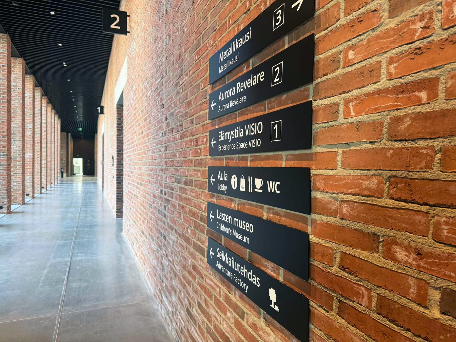 Uuden museo- ja tiedekeskuksen valoisa sisätila, jossa näkyy modernia arkkitehtuuria ja viimeisteltyjä pintamateriaaleja sekä opasteet.